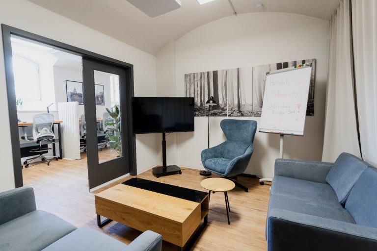 Lounge Meetingraum Moderne Büroumgebung mit Sitzgelegenheiten, TV und Flipchart.