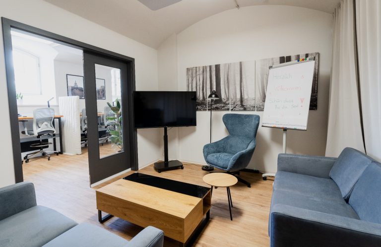 Meetingraum Gemütlicher Aufenthaltsraum mit grauen Sofas, Tisch und Stehlampe. Holzfußboden.