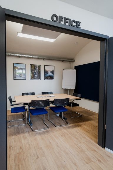 Blick in ein Büro mit einem Tisch, Stühlen und einer Präsentationswand.