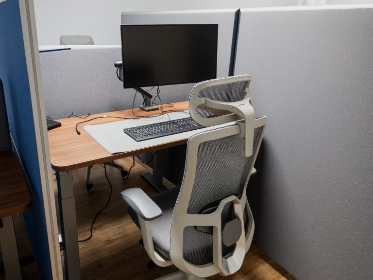 Arbeitsplatz mit Monitor, Tastatur und ergonomischem Stuhl in einem hellen Raum.
