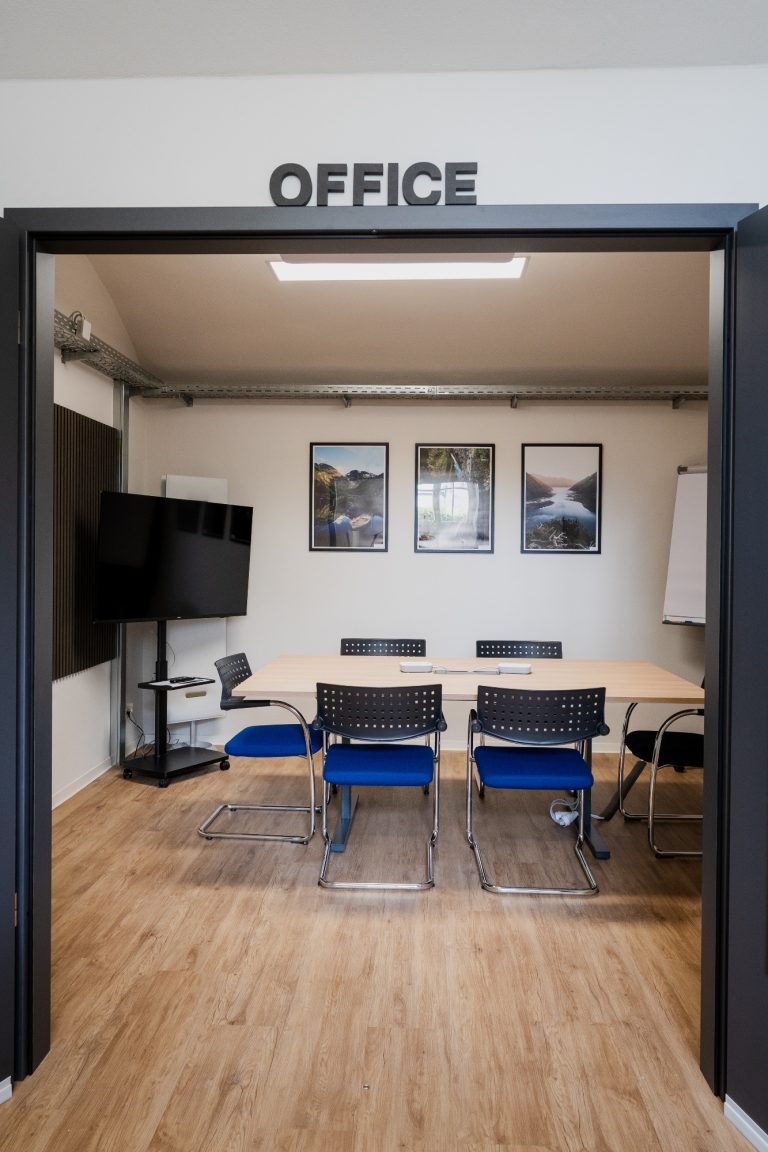 Meetingraum Office Büro mit Tisch, Stühlen, Fernseher und mehreren Bildern an der Wand.