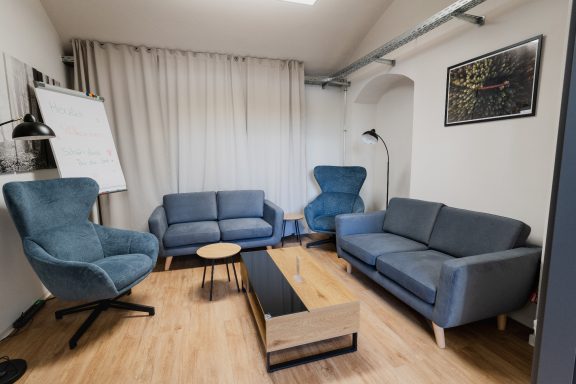 Moderne Sitzecke mit blauen Sesseln, einem Sofa und einem niedrigen Tisch in einem hellen Raum.